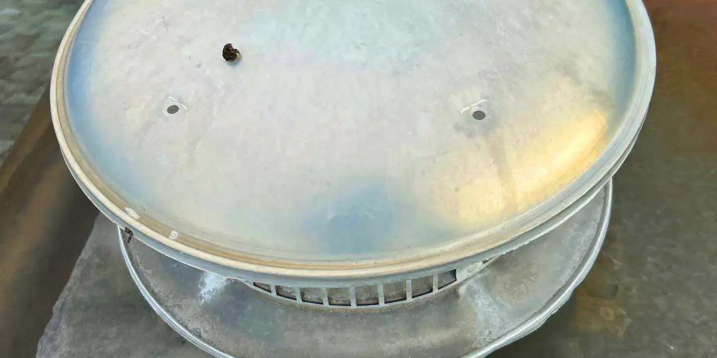 Hail damage on a vent Metal roof vent cap with hail dents on a residential roof, showing impact marks and light rust stains.