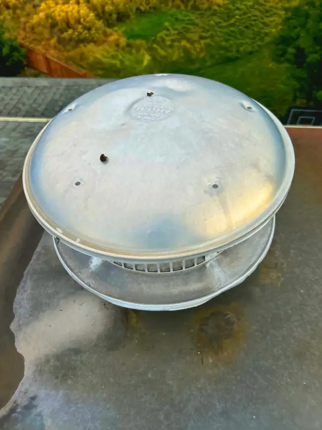 Hail damage on a vent Metal roof vent cap with hail dents on a residential roof, showing impact marks and light rust stains.