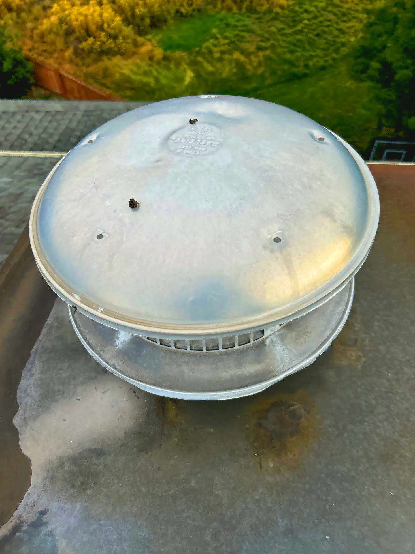 Metal roof vent cap with hail dents on a residential roof, showing impact marks and light rust stains.