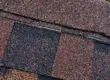 Close-up of asphalt roof shingles showing slight granule loss along the ridge cap, illustrating common granule shedding after installation