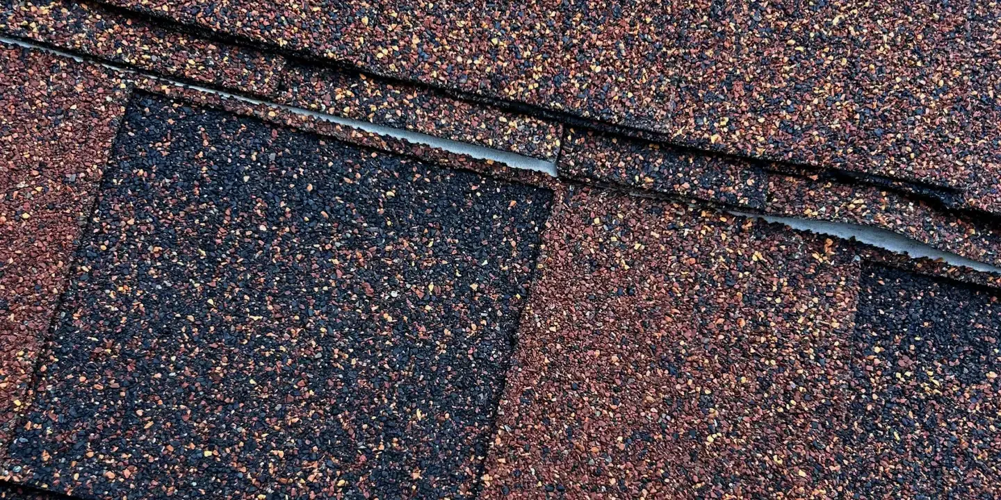 Granule Loss on New Asphalt Shingles Close-up of asphalt roof shingles showing slight granule loss along the ridge cap, illustrating common granule shedding after installation