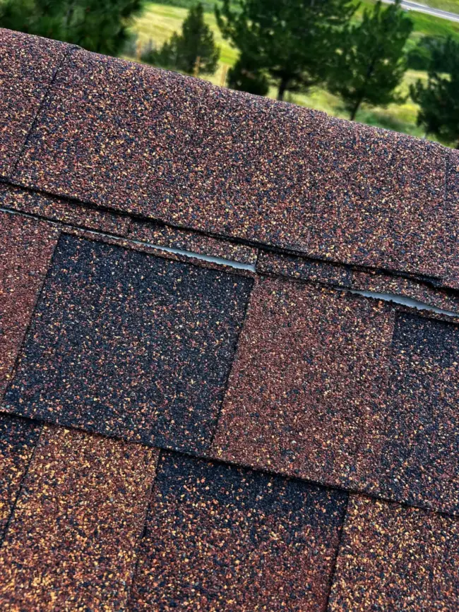 Granule Loss on New Asphalt Shingles Close-up of asphalt roof shingles showing slight granule loss along the ridge cap, illustrating common granule shedding after installation