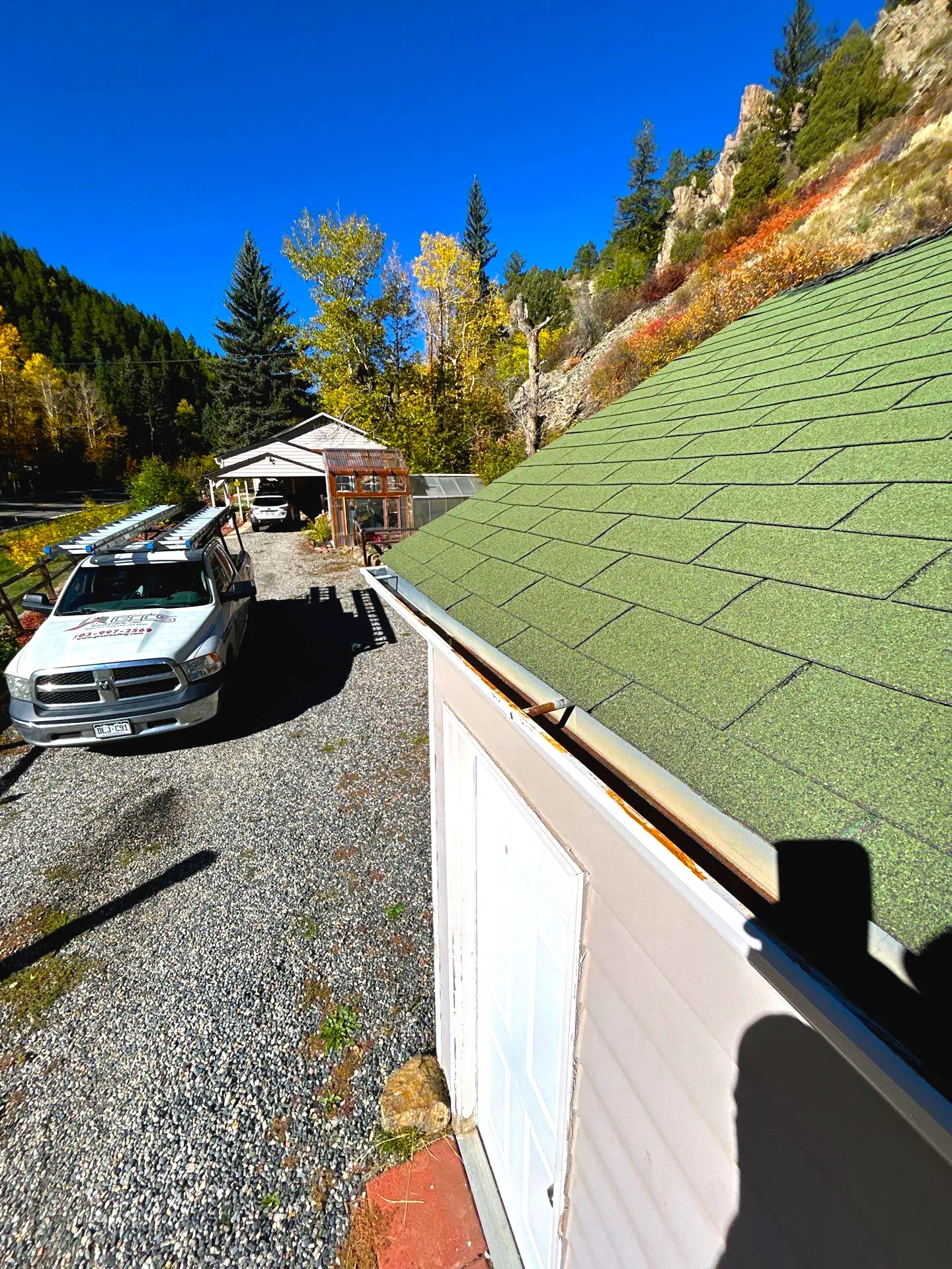 Misaligned, rusting metal gutter along the edge of a green asphalt-shingle roof.