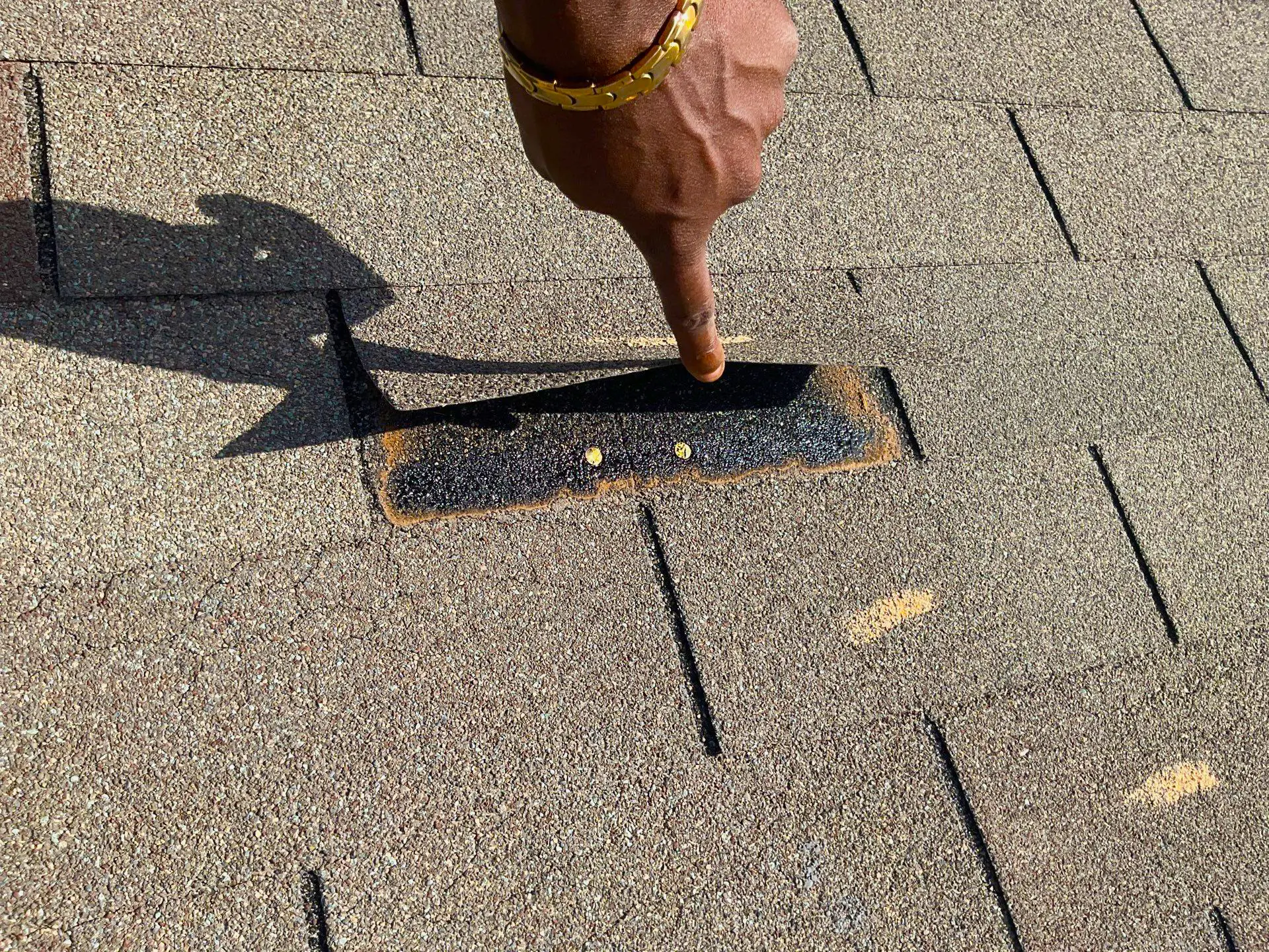 Shingle lifted to reveal an incorrectly placed nail, positioned too high above the nailing strip.