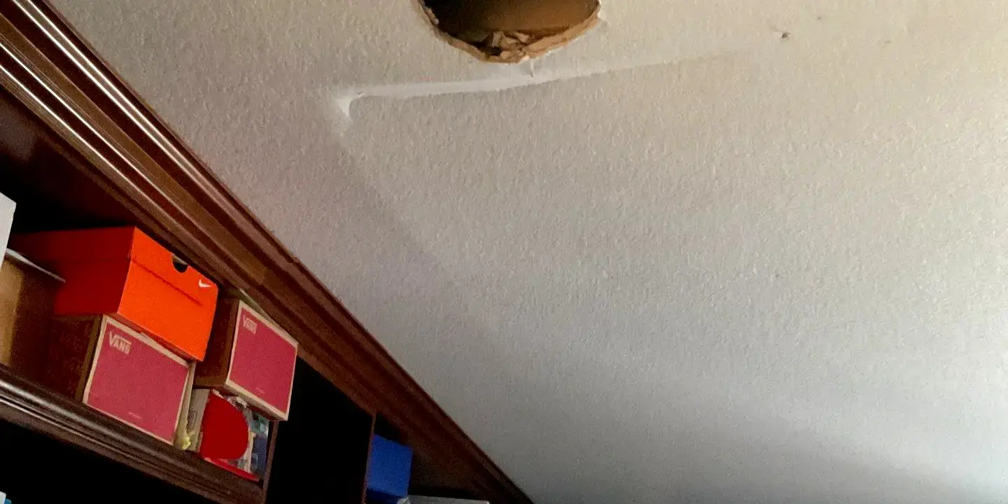 Hole and crack after roof damage Hole and crack in a bedroom ceiling from a water leak after roof damage, showing interior moisture intrusion and the need for urgent roof repair.