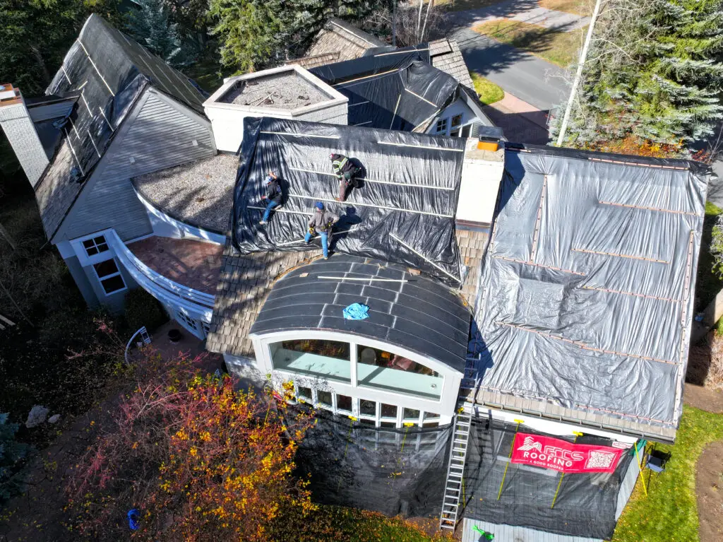Roofers installing protective tarps during a complex residential roof repair project