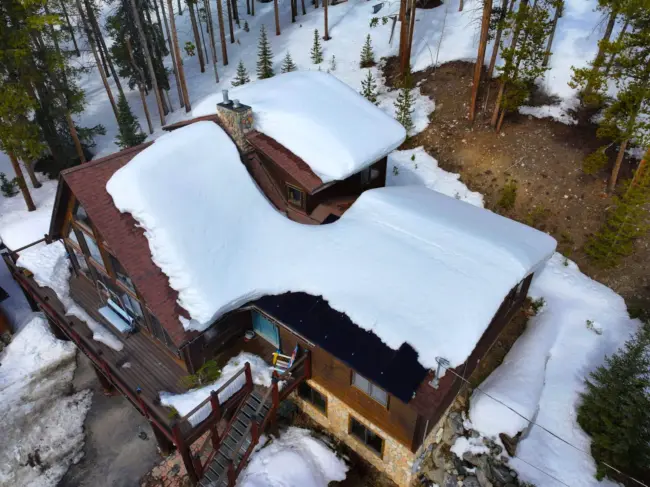 Snow-covered cabin roof Snow-covered cabin roof in Littleton, CO showing heavy snow buildup and potential for winter roof leaks.