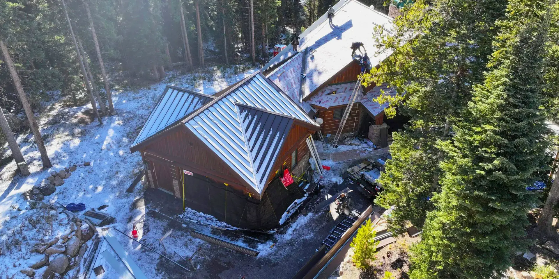 Roofing crew working Roofing crew working on the installation of a metal roof on a house surrounded by trees and light snow.