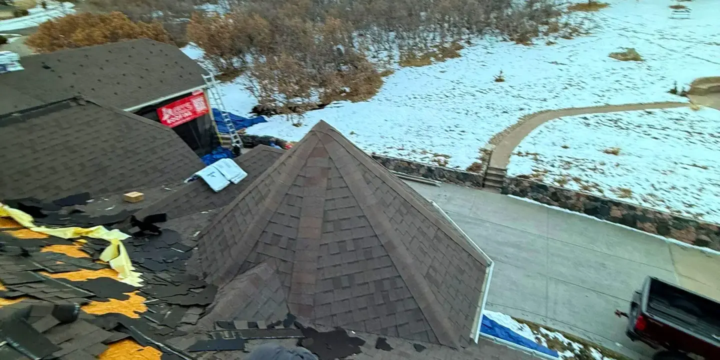Roofing technician repairing damaged shingles on a residential roof during winter in Littleton, CO