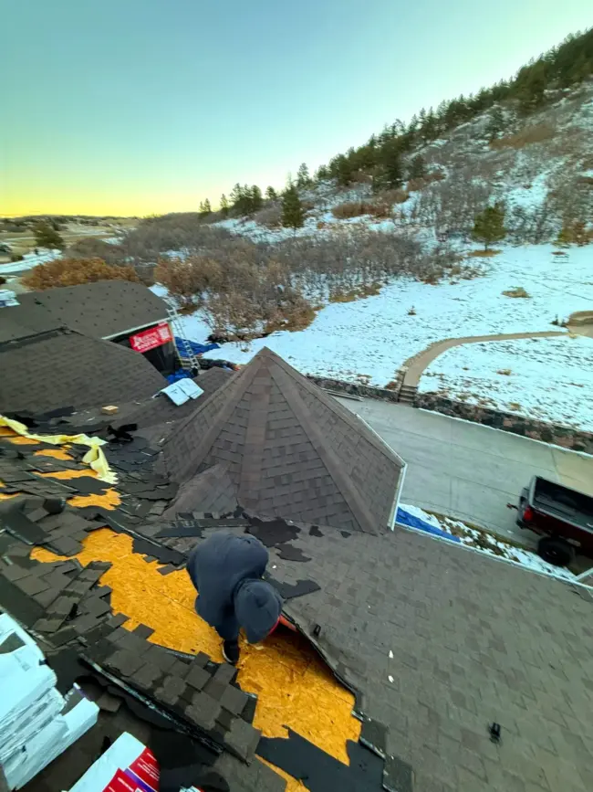 Roofing technician repairing damaged shingles on a residential roof during winter in Littleton, CO