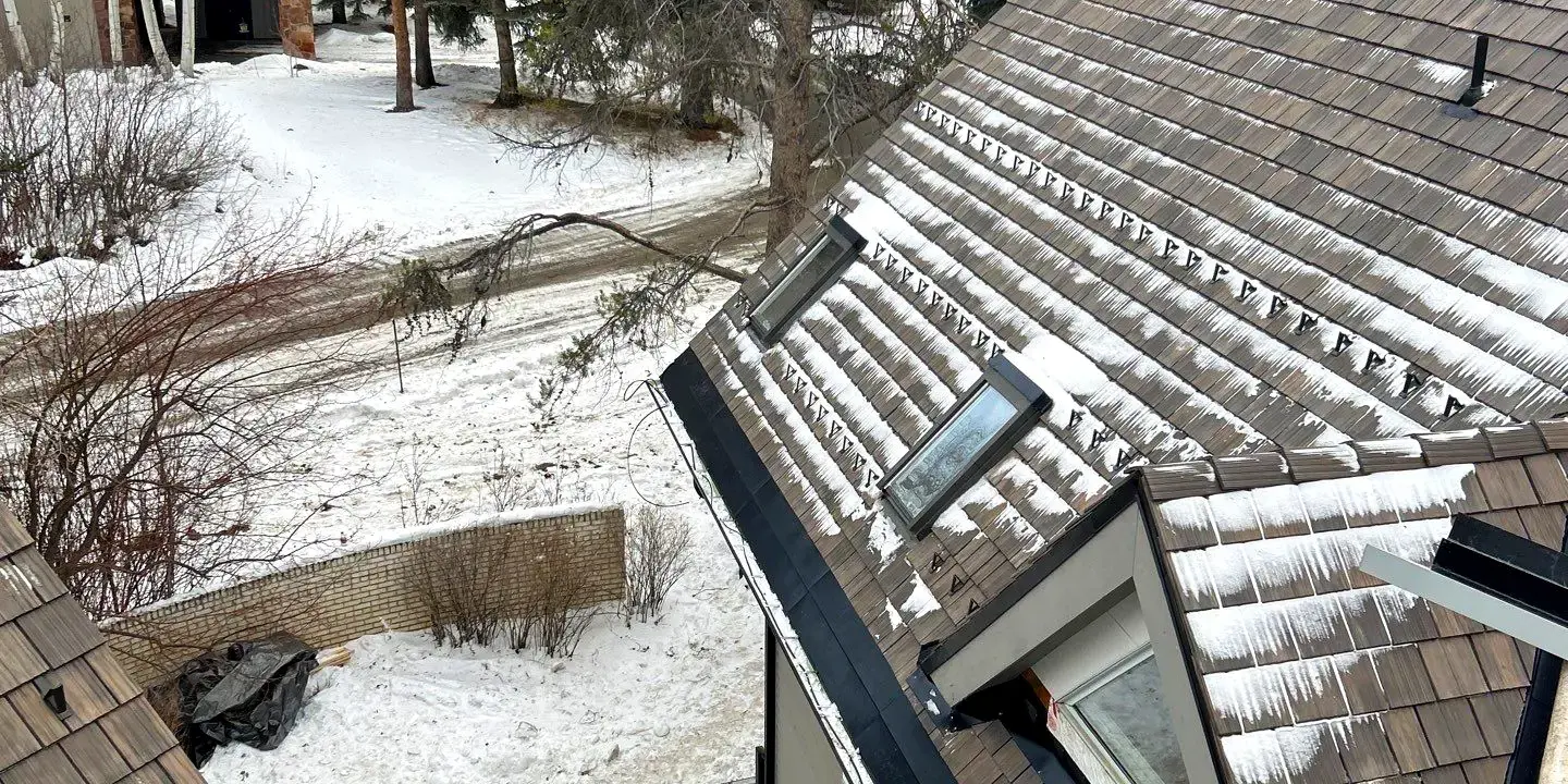 Sloped residential roof with shake-style shingles and partial snow accumulation