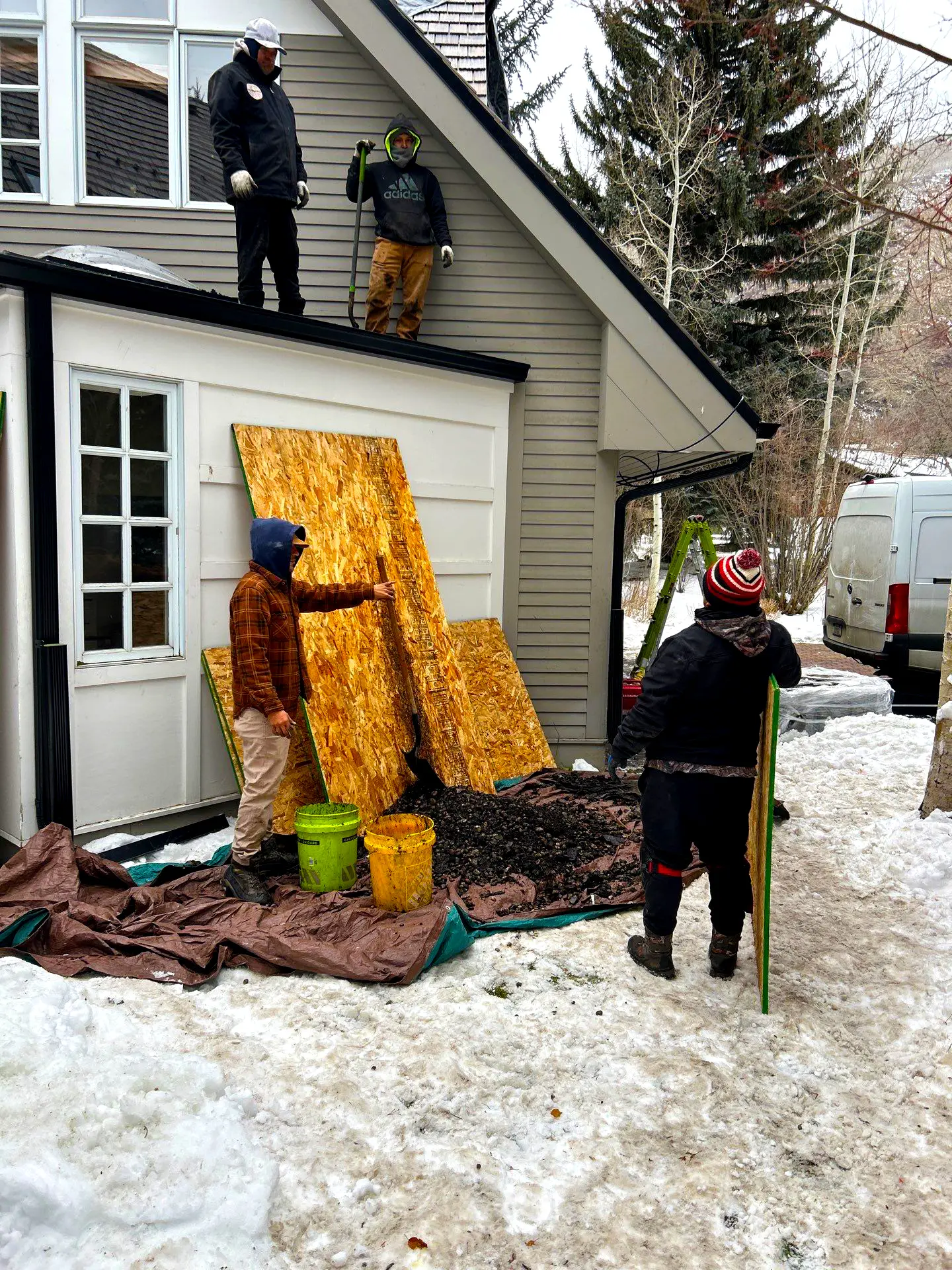 Roofing crew performing residential roof repair during winter, removing shingles and protecting the home with plywood and tarps in Colorado.