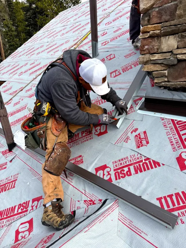 Professional roofer installing metal flashing at the base of a chimney, a critical detail to prevent leaks and ensure long-term roof durability in Littleton, Colorado.
