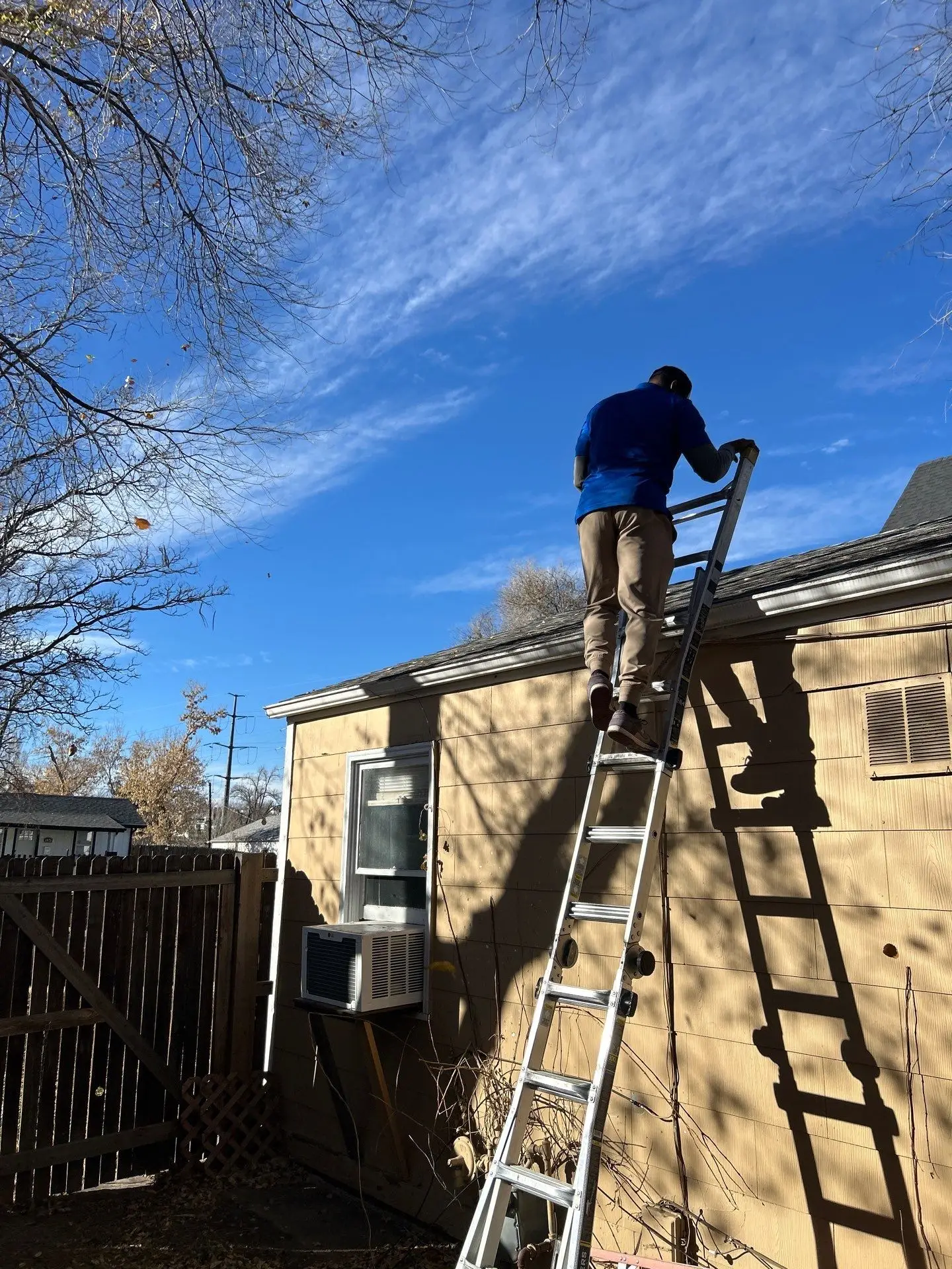 Roofing technician performing a roof inspection from a ladder on a residential home