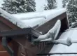 Snow-covered residential roof in a wooded area showing heavy snow accumulation.