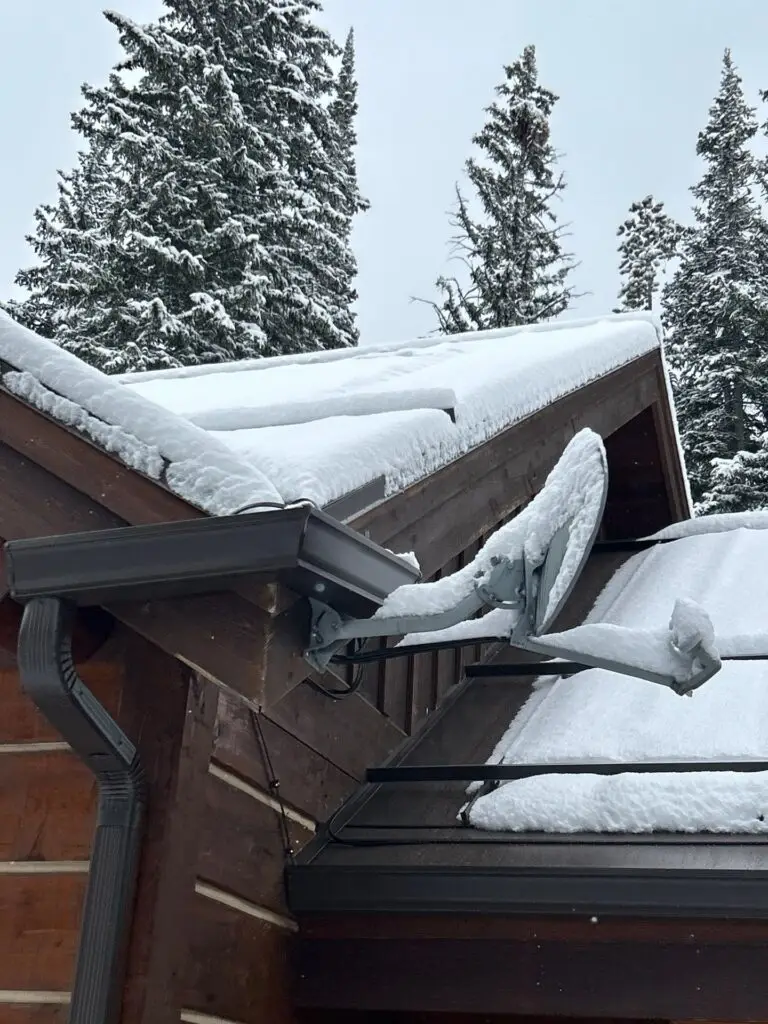 Snow-covered residential roof in a wooded area showing heavy snow accumulation.