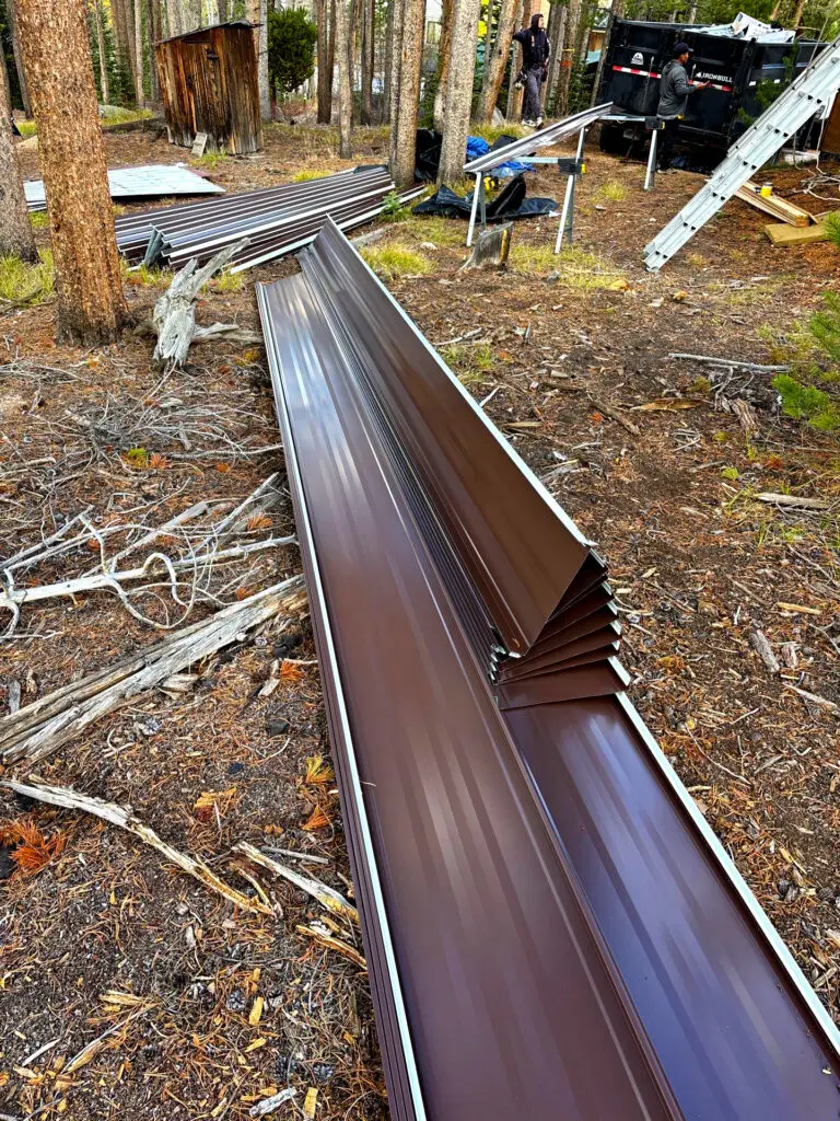 Metal roofing panels laid on the ground during a metal roof installation in a wooded area of Colorado, showing the work process of professional roofers.