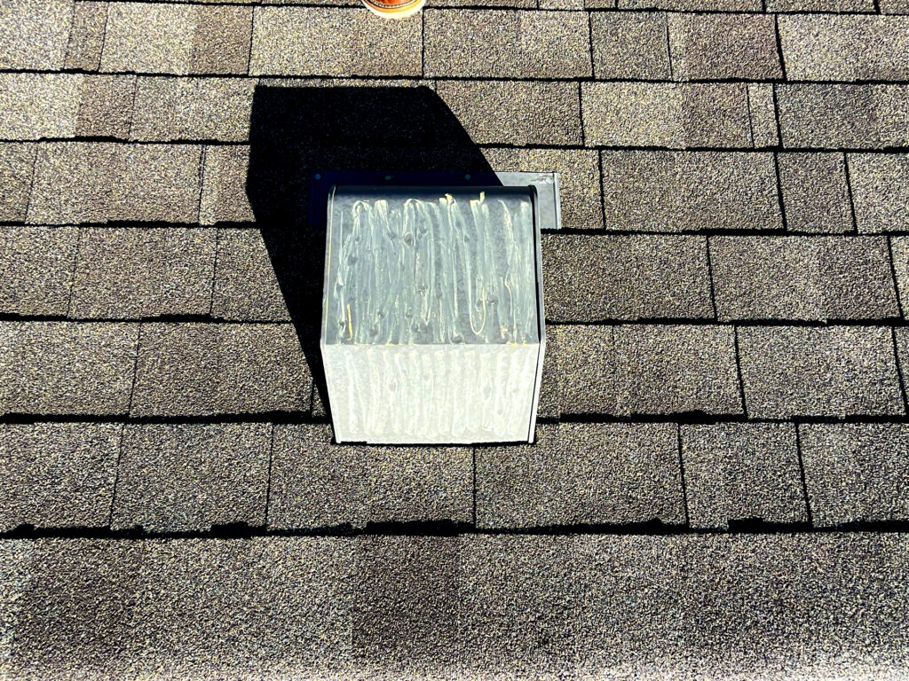 Close-up of roof vent on asphalt shingle roof with worn sealant, showing a common area vulnerable to leaks and storm-related damage.