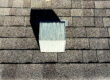 Close-up of roof vent on asphalt shingle roof with worn sealant, showing a common area vulnerable to leaks and storm-related damage.