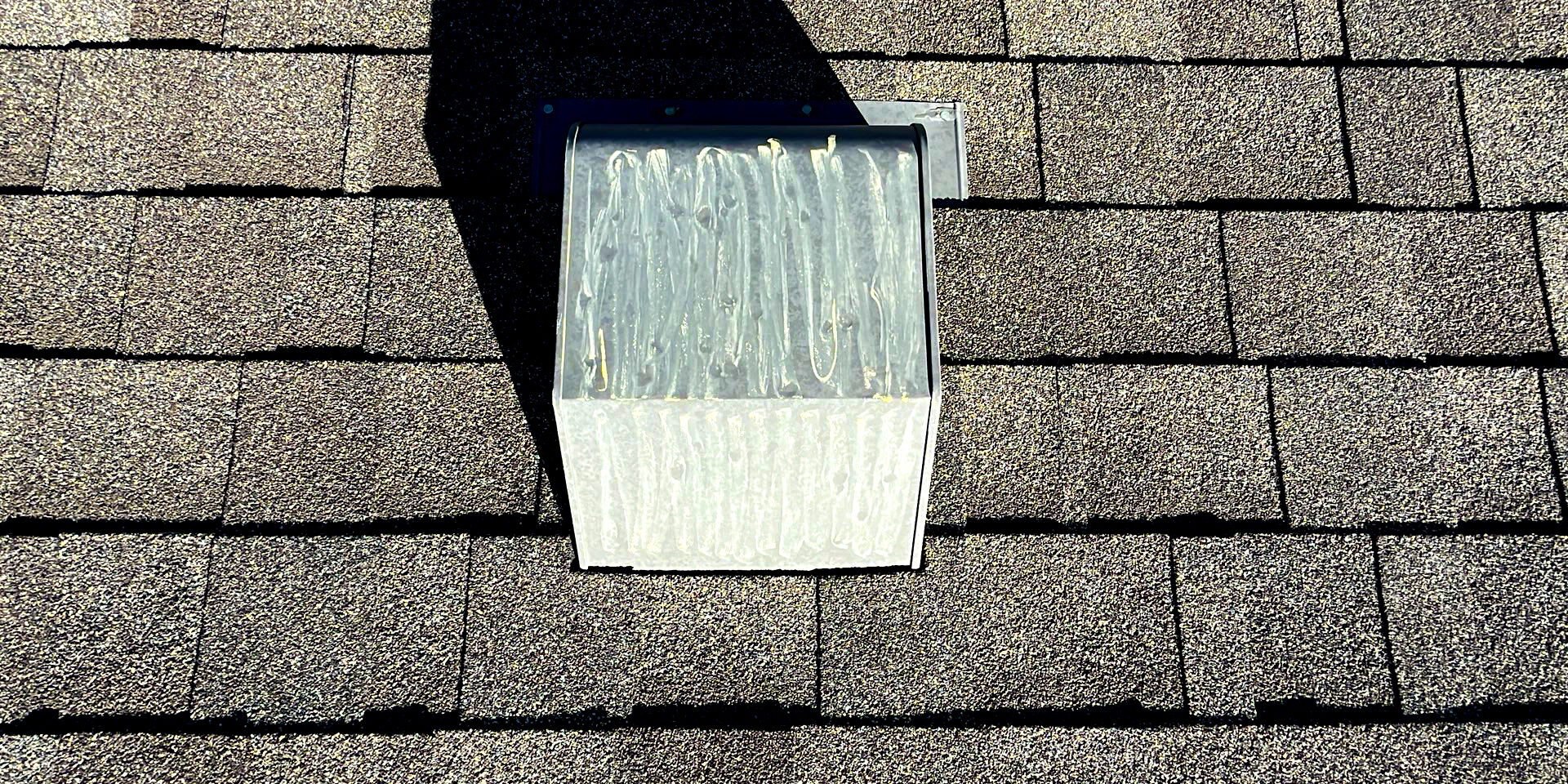 Close-up of roof vent on asphalt shingle roof with worn sealant, showing a common area vulnerable to leaks and storm-related damage.