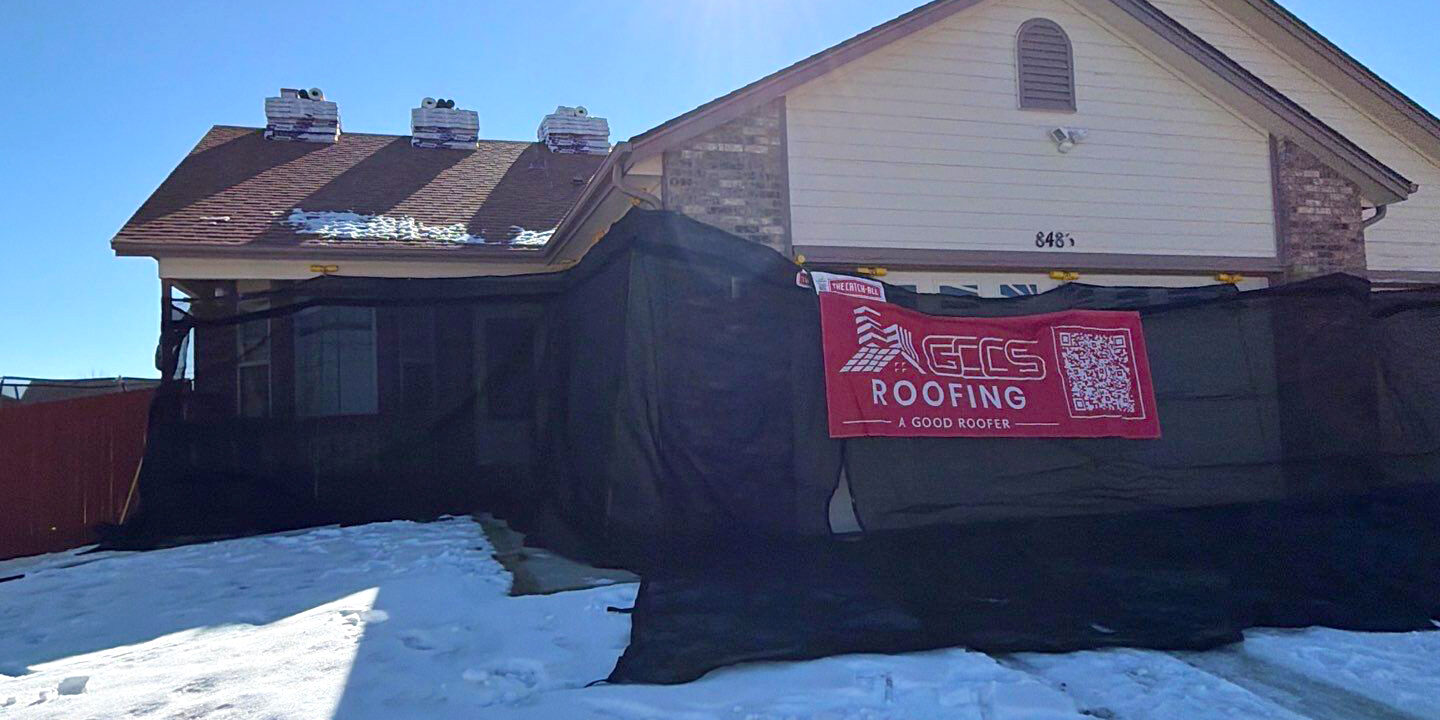 The Catch All System installed during a residential roofing project in winter, featuring black protective mesh surrounding the home and snow on the ground to protect the property during roof work.