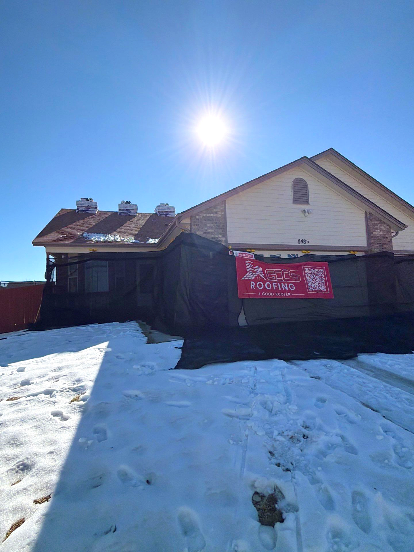 The Catch All System installed during a residential roofing project in winter, featuring black protective mesh surrounding the home and snow on the ground to protect the property during roof work.