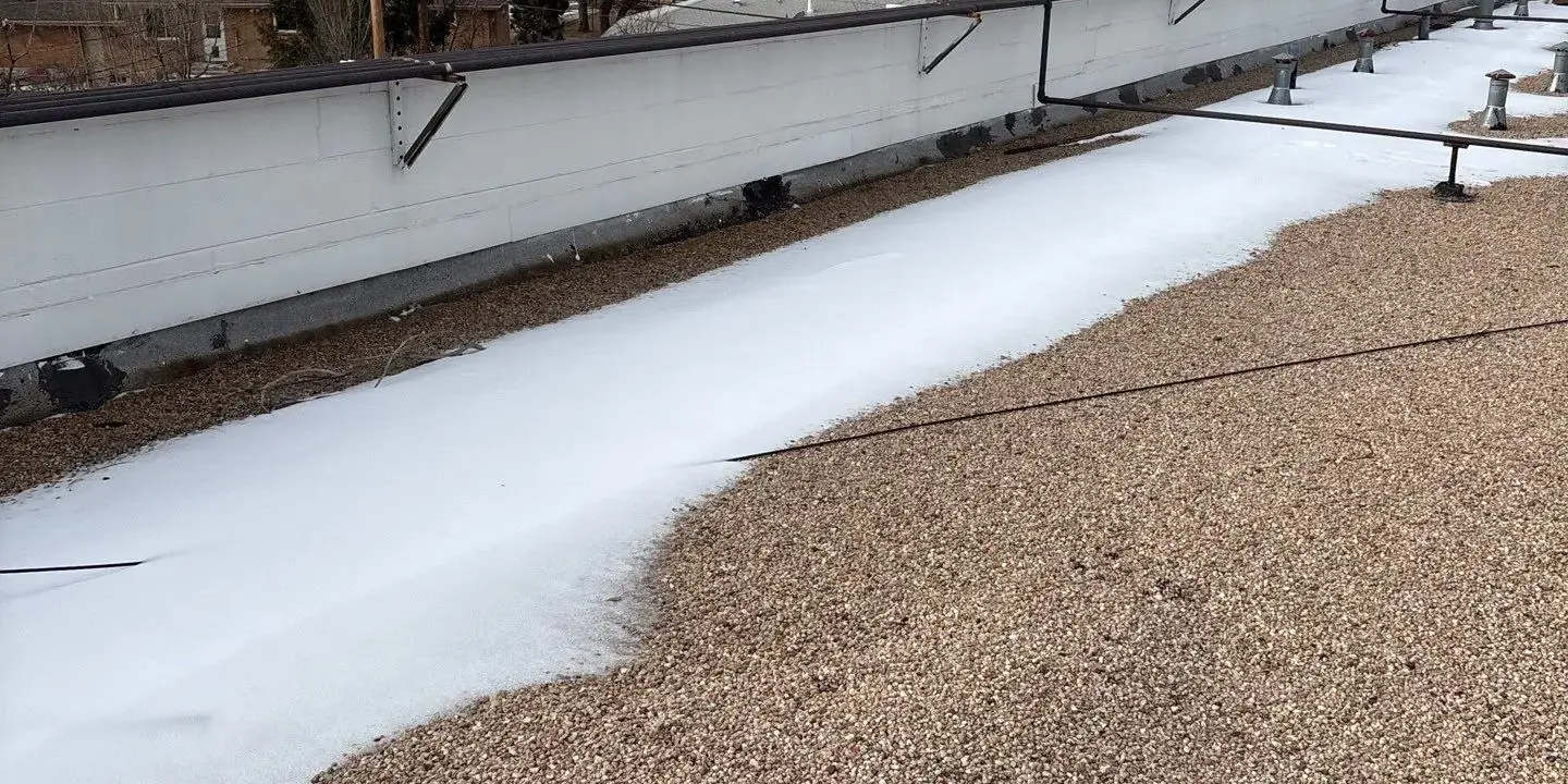Commercial flat roof Commercial flat gravel roof with partial snow accumulation along the parapet, highlighting winter conditions that can impact drainage and roofing performance.