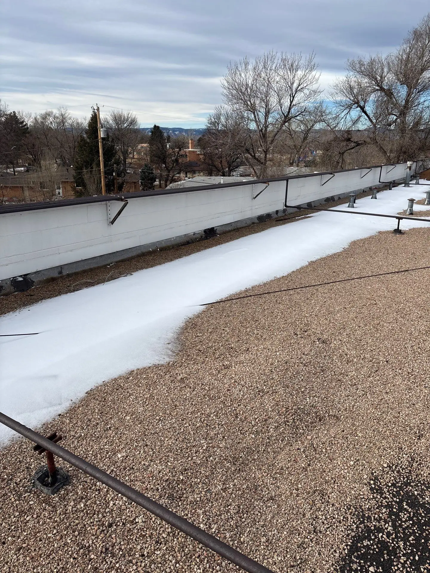 Commercial flat gravel roof with partial snow accumulation along the parapet, highlighting winter conditions that can impact drainage and roofing performance.