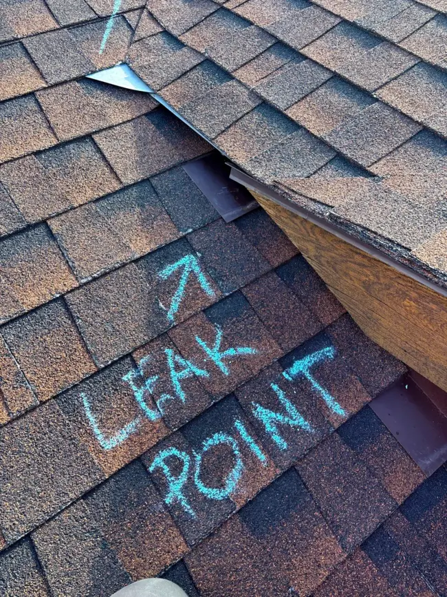 Close-up of asphalt shingle roof showing damage and a marked leak point during a professional roof repair inspection in Littleton, CO.