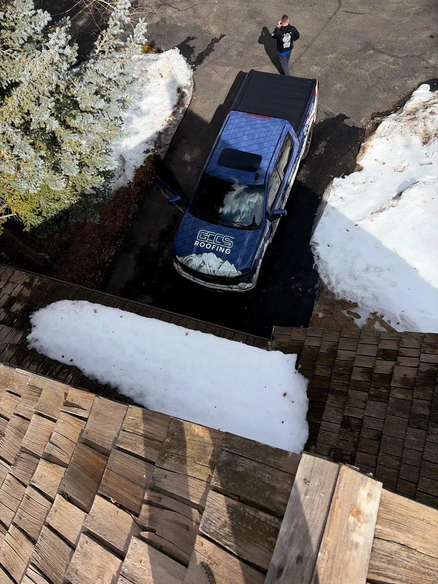GCCS Roofing truck parked in a snowy driveway in Littleton, CO while a roofer performs a roof inspection