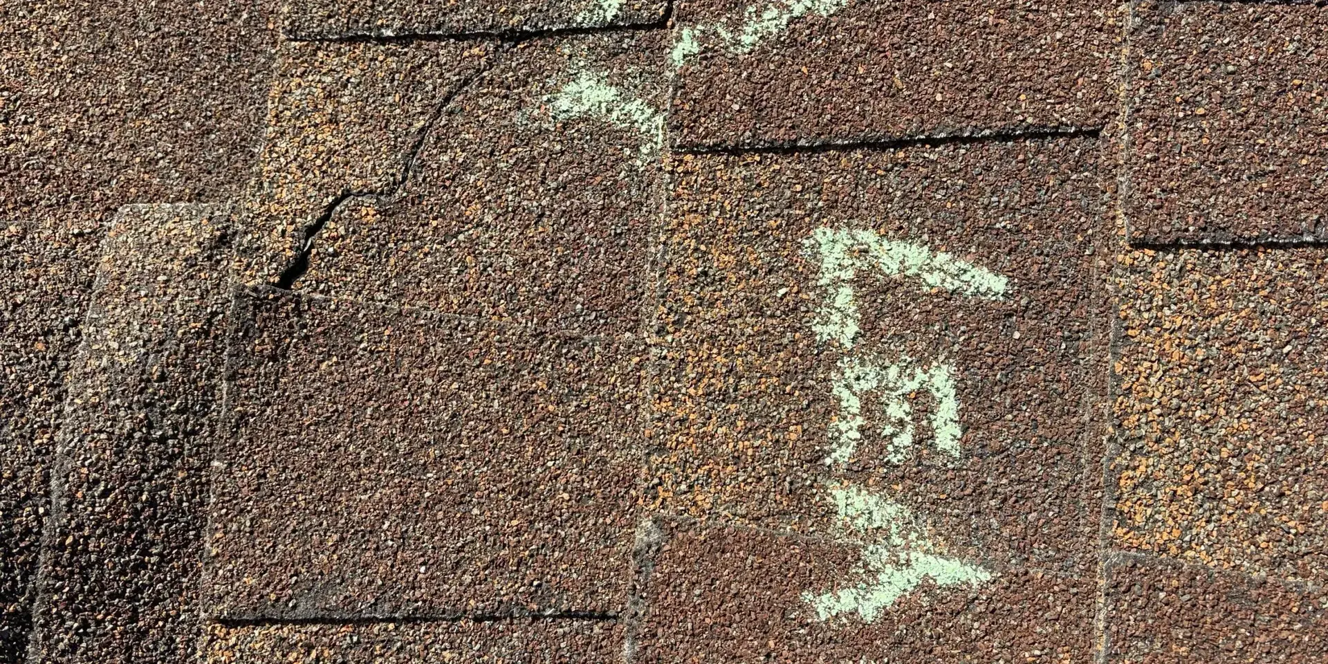 Close-up of asphalt roof shingles with hail impact damage, highlighting cracks and wear illustrating why homeowners upgrade to Class 4 impact-resistant roofing.