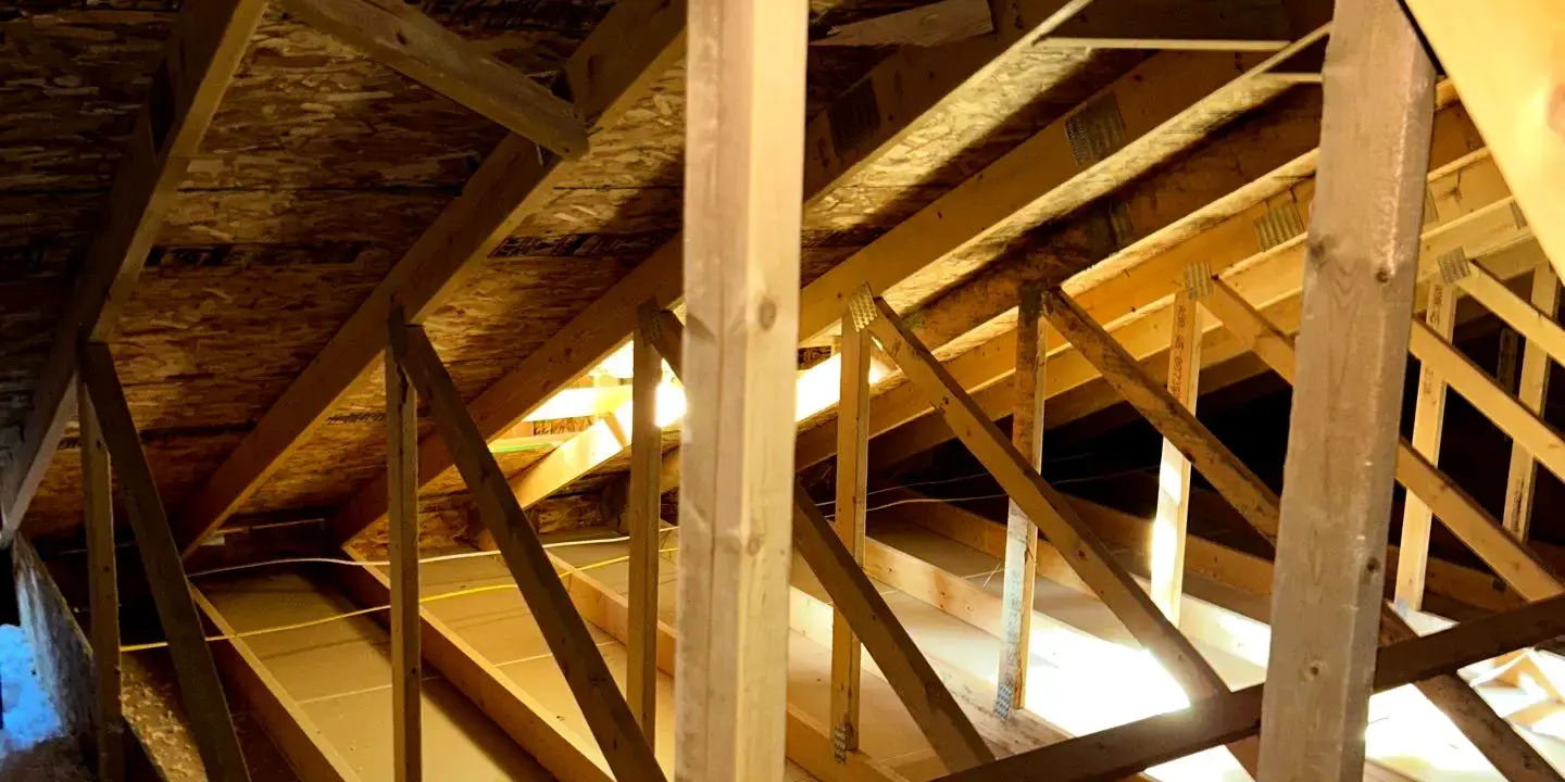 Interior view of a residential attic showing wooden roof trusses, roof decking, and insulation, illustrating structural framing and potential areas for hidden roof leaks or attic water damage.