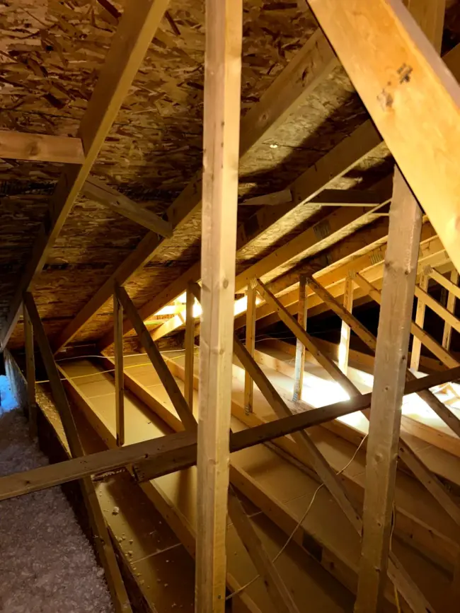 Interior view of a residential attic showing wooden roof trusses, roof decking, and insulation, illustrating structural framing and potential areas for hidden roof leaks or attic water damage.