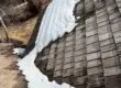 Snow accumulation on a residential shingle roof showing uneven melting patterns and potential winter damage to the roofing system