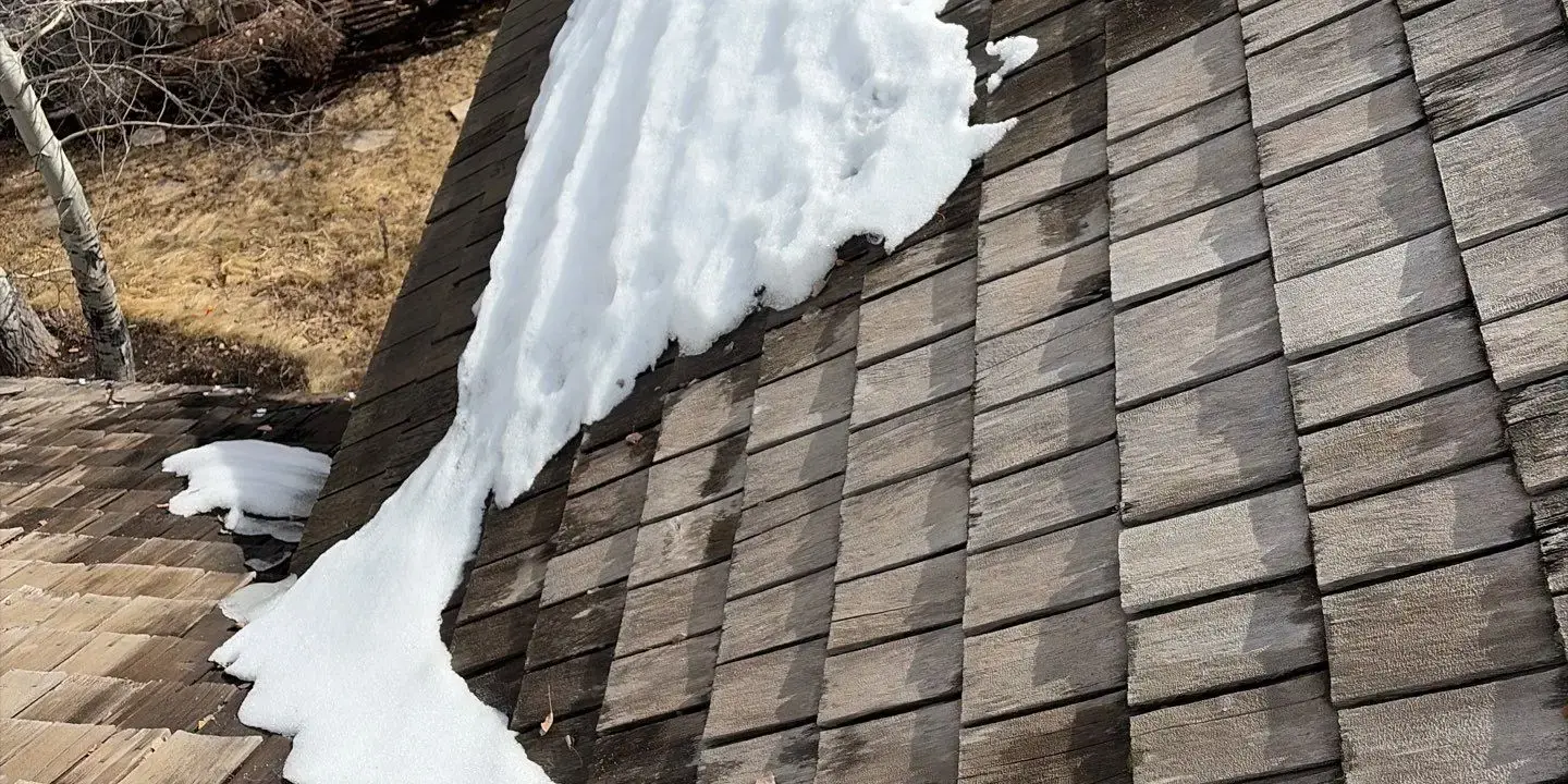 Snow melting on a wood shingle roof Snow accumulation on a residential shingle roof showing uneven melting patterns and potential winter damage to the roofing system