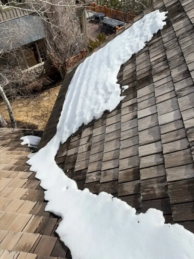 Snow melting on a wood shingle roof Snow accumulation on a residential shingle roof showing uneven melting patterns and potential winter damage to the roofing system