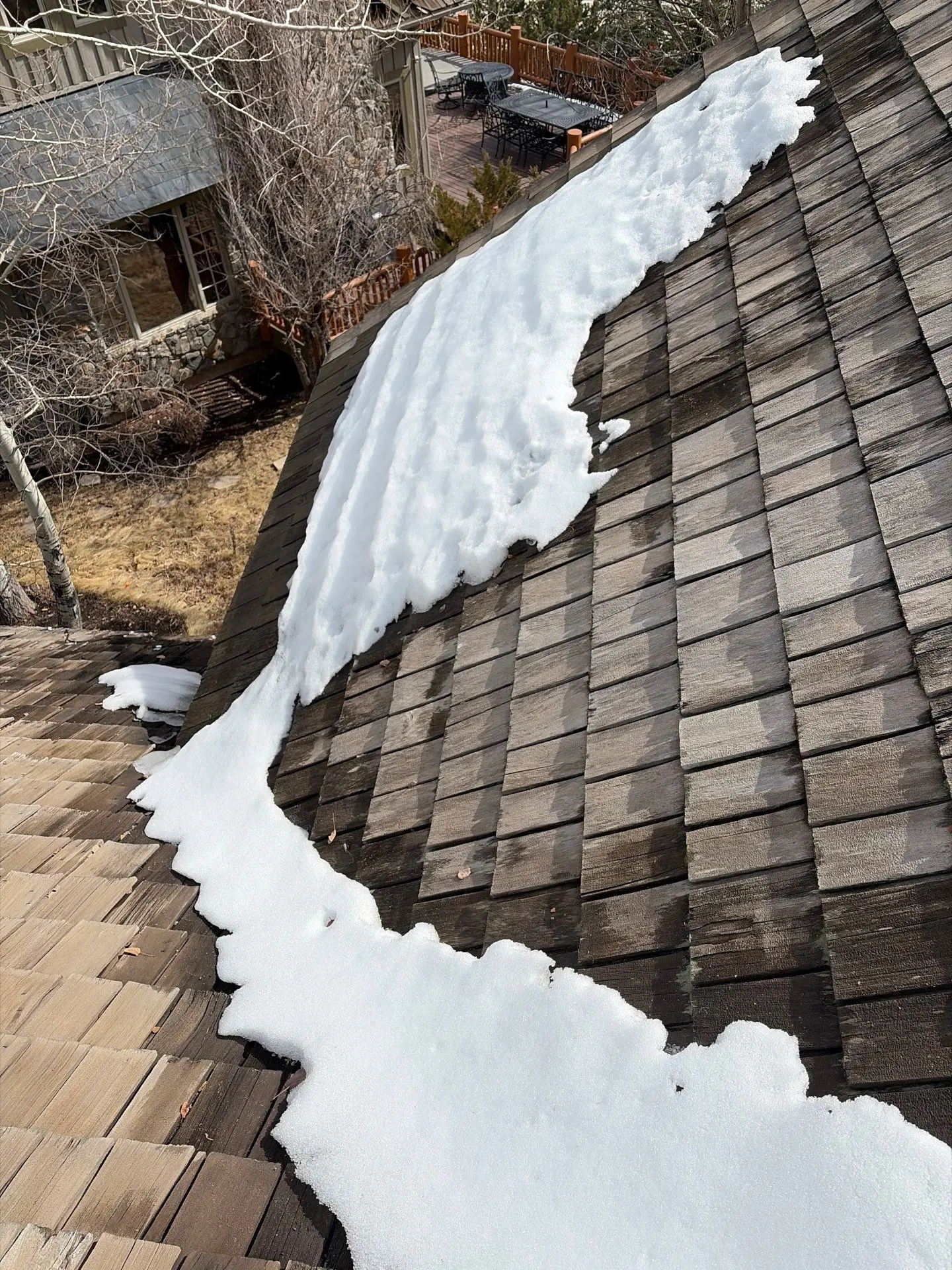 Snow accumulation on a residential shingle roof showing uneven melting patterns and potential winter damage to the roofing system