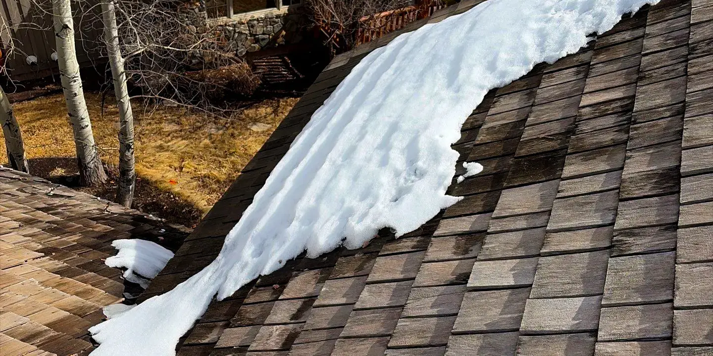 Snow melting on a wood shingle roof of a residential home, showing wet areas where roof leaks can occur after winter in Littleton, Colorado.