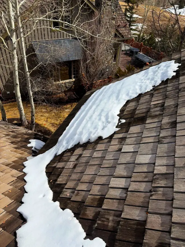Snow melting on a wood shingle roof of a residential home, showing wet areas where roof leaks can occur after winter in Littleton, Colorado.