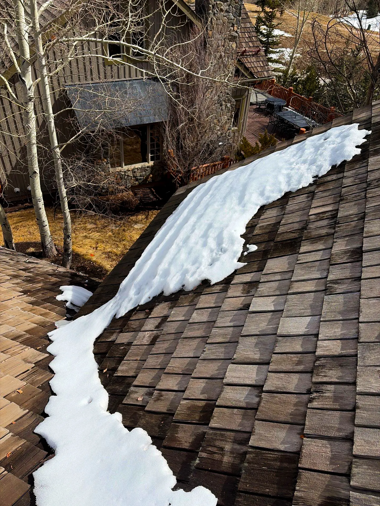 Snow melting on a wood shingle roof of a residential home, showing wet areas where roof leaks can occur after winter in Littleton, Colorado.