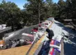 Residential roofing installation in Colorado with materials and crew positioned on the roof, surrounded by pine trees under a clear blue sky.