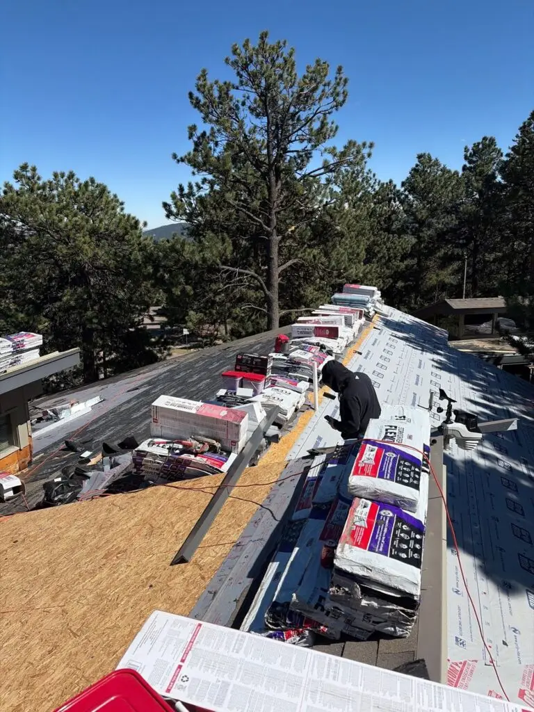 Residential roofing installation in Colorado with materials and crew positioned on the roof, surrounded by pine trees under a clear blue sky.