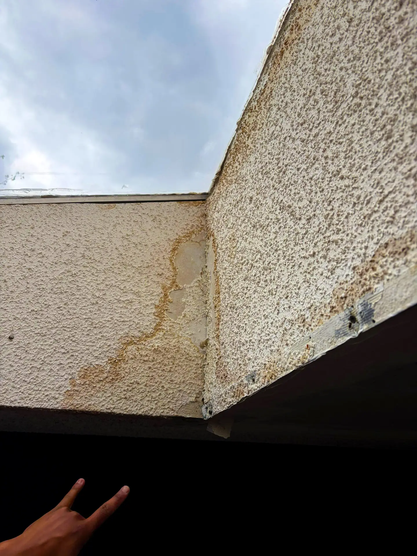 Water infiltration damage on textured exterior wall near the roofline, possible sign of a roofing leak.