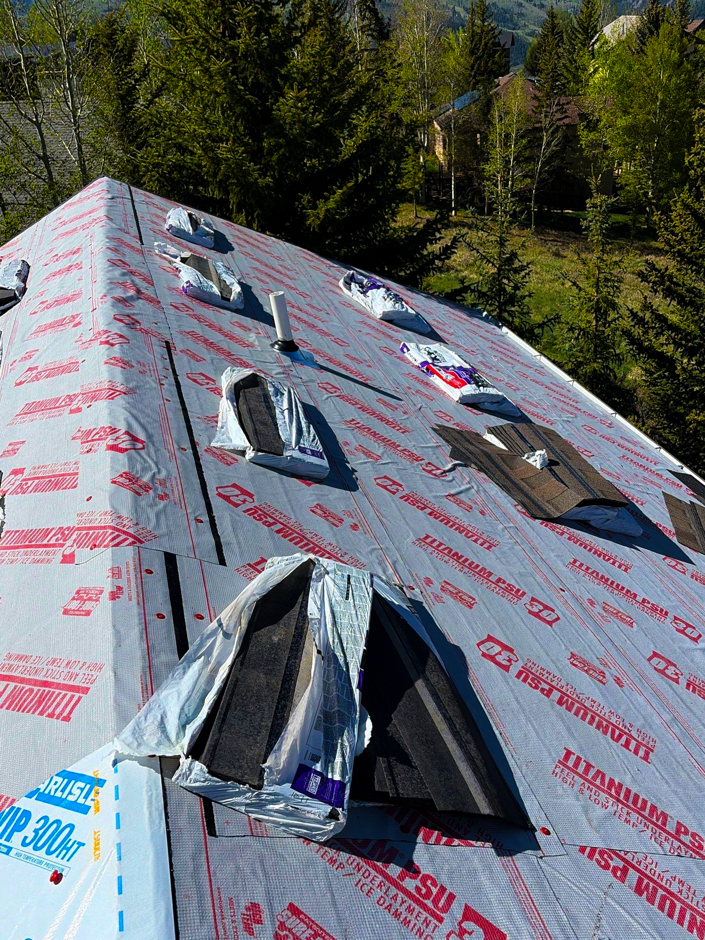 Roof replacement in progress with synthetic underlayment and new shingles being installed to protect a residential property in a wooded area.