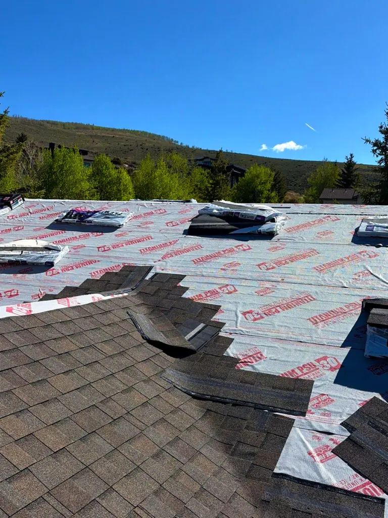 Installation of asphalt shingles and synthetic underlayment on a residential mountain property roof.