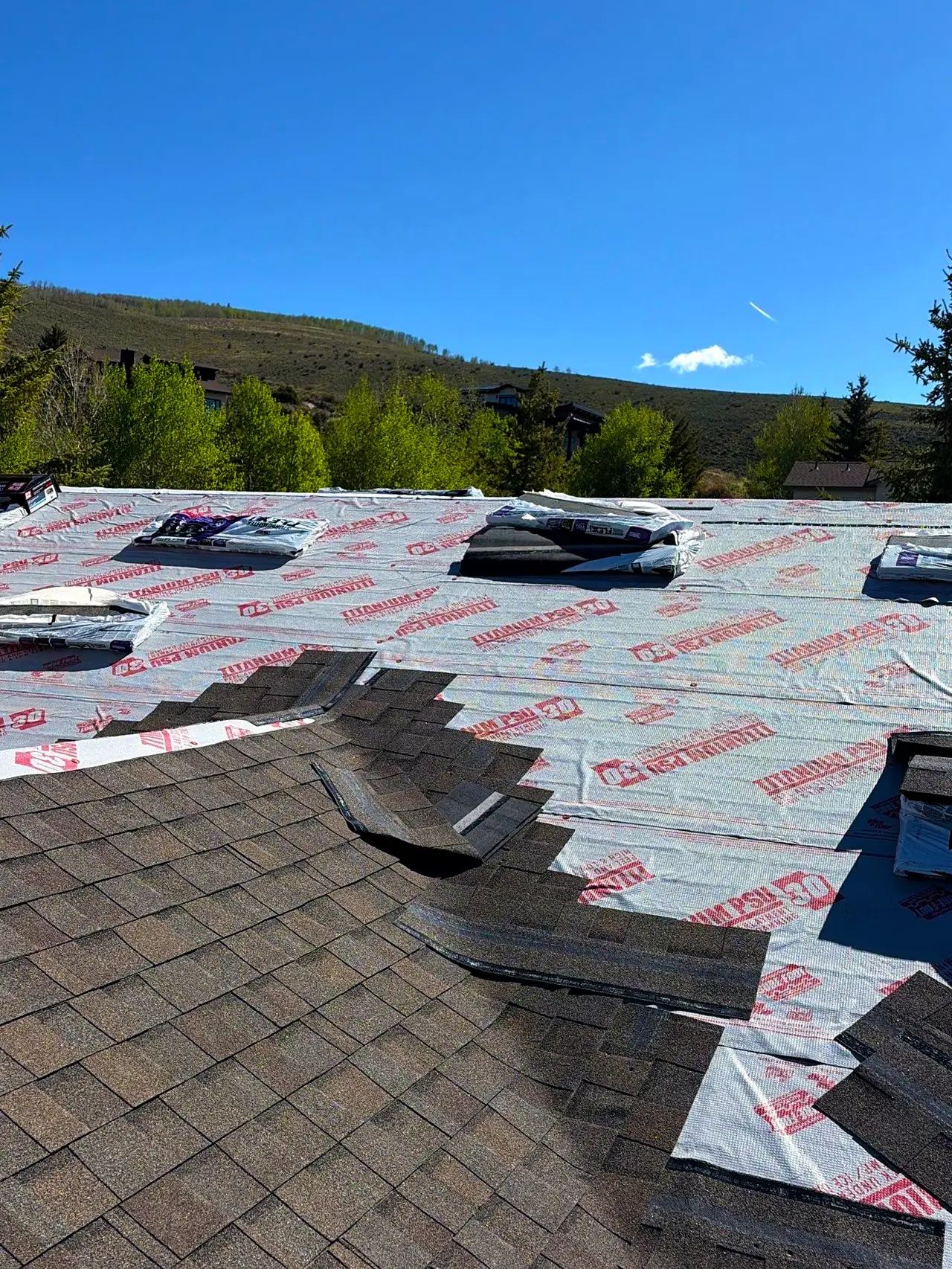 Installation of asphalt shingles and synthetic underlayment on a residential mountain property roof.