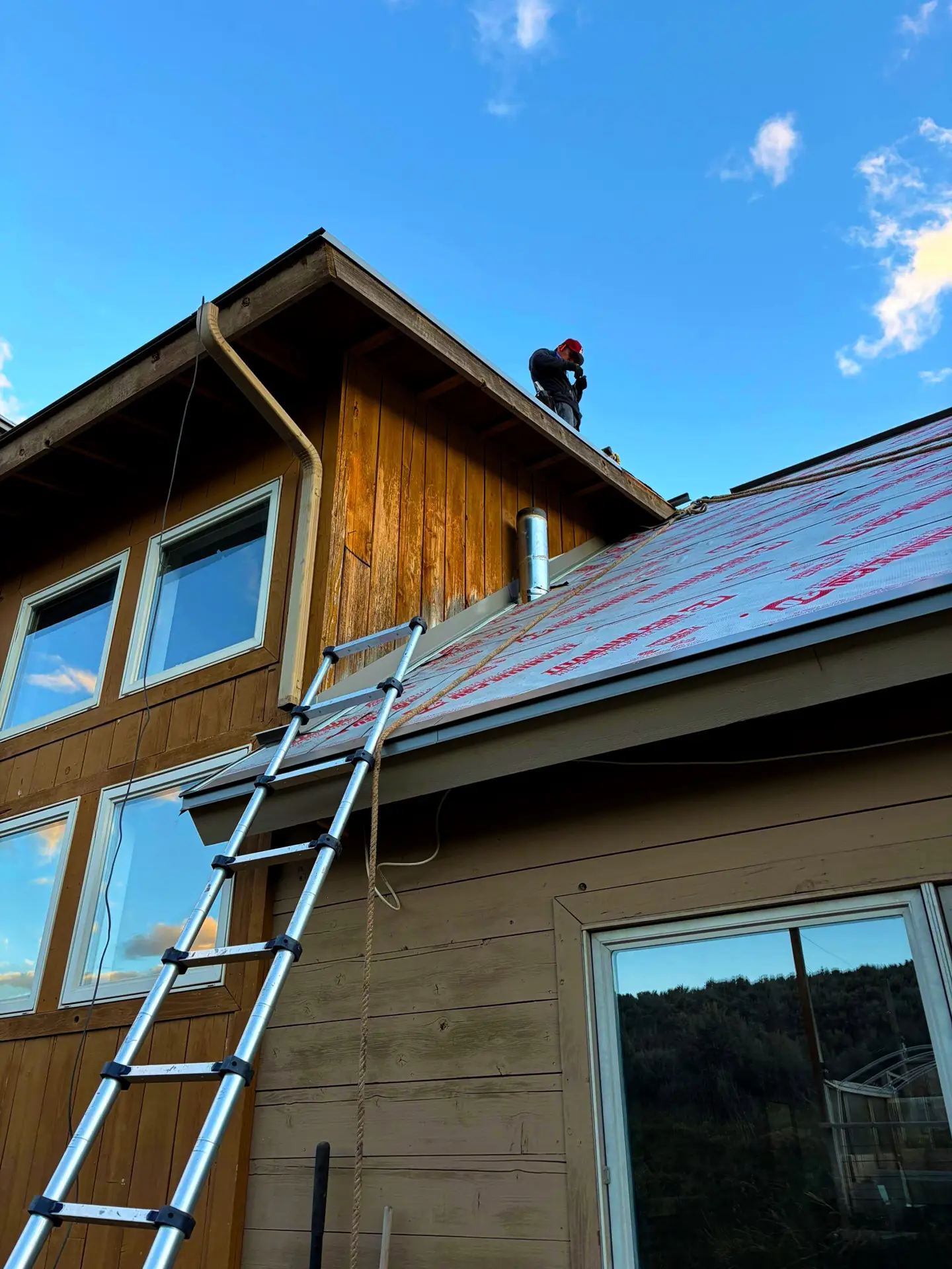 Roofer installing metal roofing panels over protective underlayment on a residential home in Colorado.