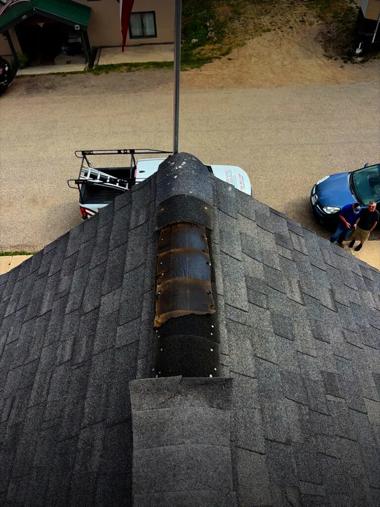 Close-up roof inspection showing damaged chimney flashing and worn shingles on a residential roof.