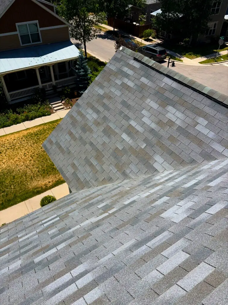 Steep gray asphalt shingle roof viewed from above, showing clean roof lines and nearby residential homes on a sunny day.