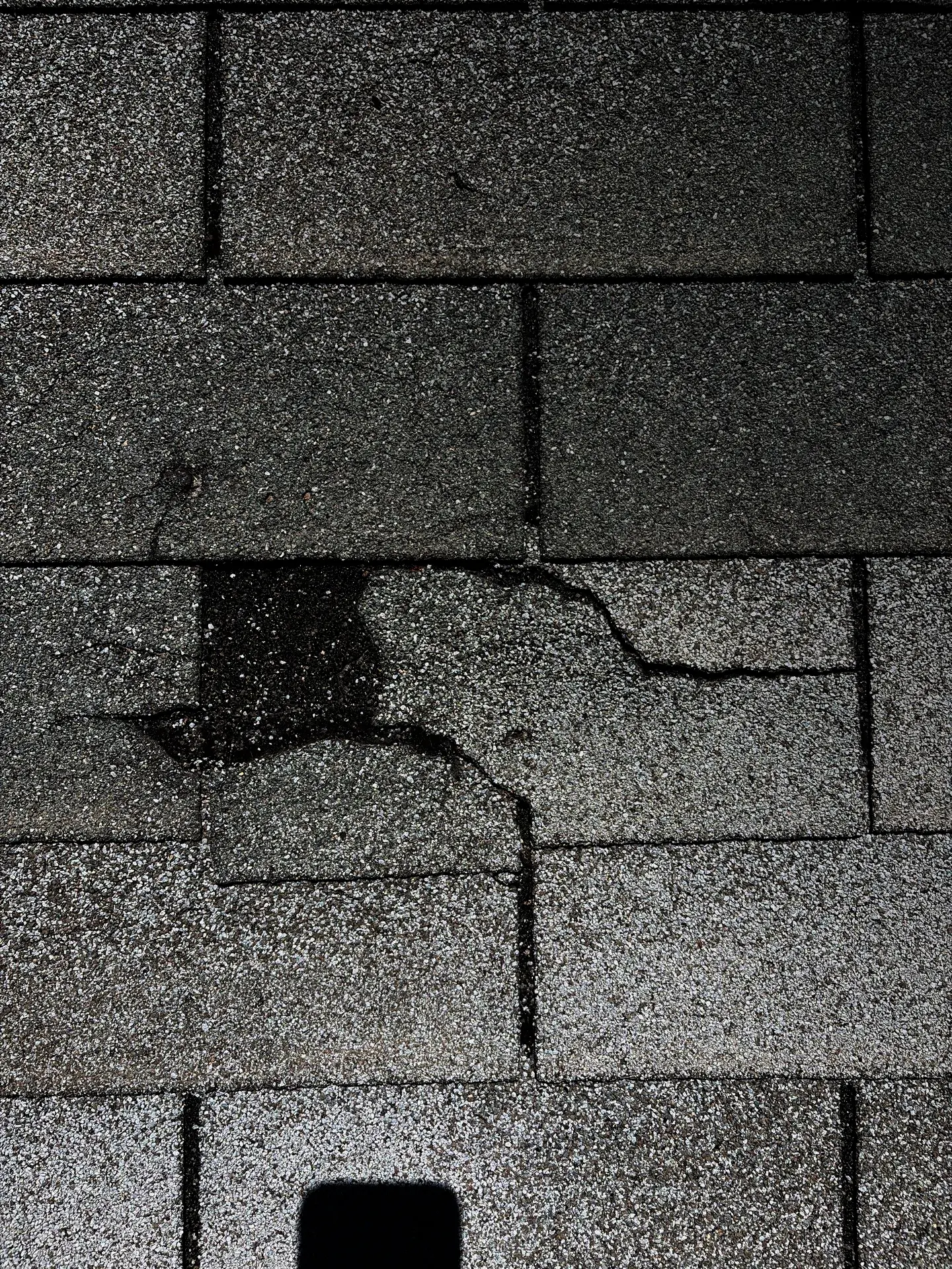 damaged asphalt shingles with cracks, granule loss, and a dark moisture stain indicating the need for emergency roof repair.